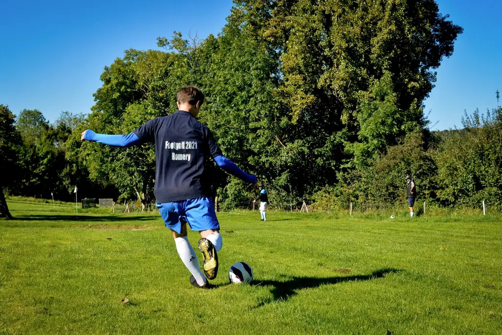 Un joueur frappe le ballon de Footgolf dans un parc arboré